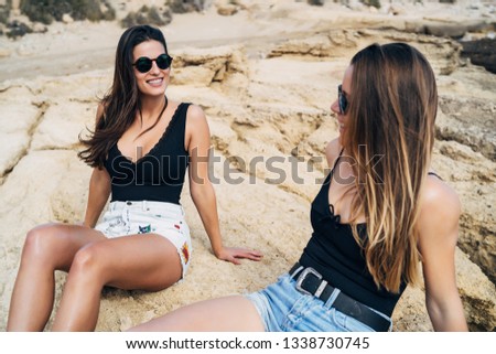 Two young women sitting on the seashore enjoying the summer holidays in the beach