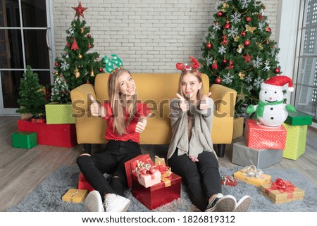 Two young women sitting on the floor raising her thumb up with a smiling faces in a room decorated for Christmas