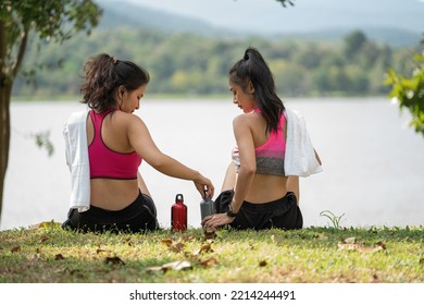 Two Young Women Sitting At The Park And Relaxing After Jogging Outdoors.