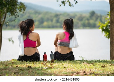 Two Young Women Sitting At The Park And Relaxing After Jogging Outdoors.