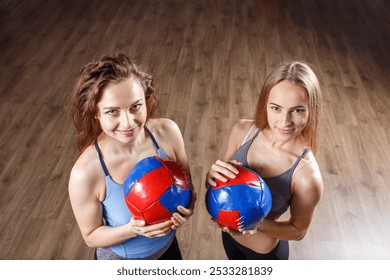 Two young women smile while holding colorful medicine balls, showcasing their enthusiasm for sports and fitness. - Powered by Shutterstock