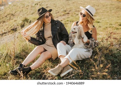 Two Young Women Spend Time Together In Nature. Same Sex Couple Relaxing And Laughing Together With The Dog Outside.