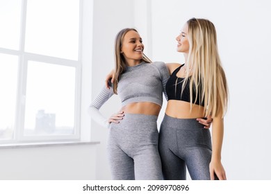 Two young women in sportswear laughing and standing arm in arm together in a gym - Powered by Shutterstock