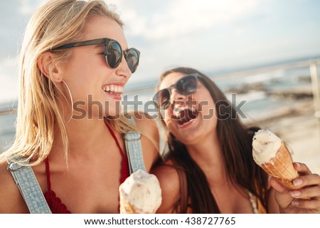 Two young women standing together laughing and eating ice cream. Happy young female friends with icecream enjoying together on a summer day.