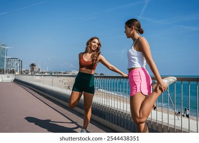 Two young women stretching legs before running on beachfront promenade in barcelona - Powered by Shutterstock