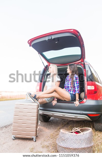 Two young women with suitcases on car\
trip. They are sitting in back of the car, resting after long ride\
and having fun. Hitchhiking and traveling by\
car