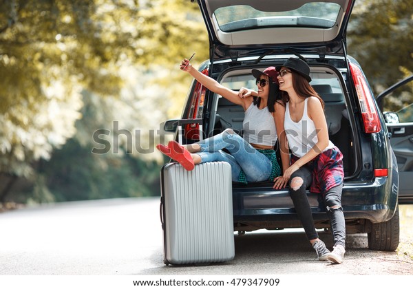 Two young\
women with suitcases on car trip.They are sitting in car back and\
resting after long ride.Taking\
selfie.