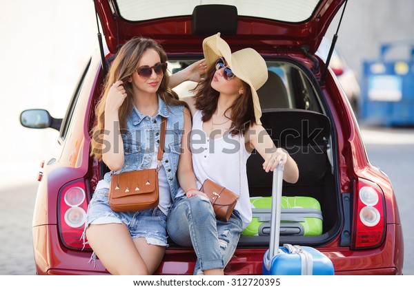 Two young women with\
suitcases. Vacation concept. Car trip. Summer vacation. Best friend\
posing with their luggage. women traveling with suitcases, sitting\
in car back