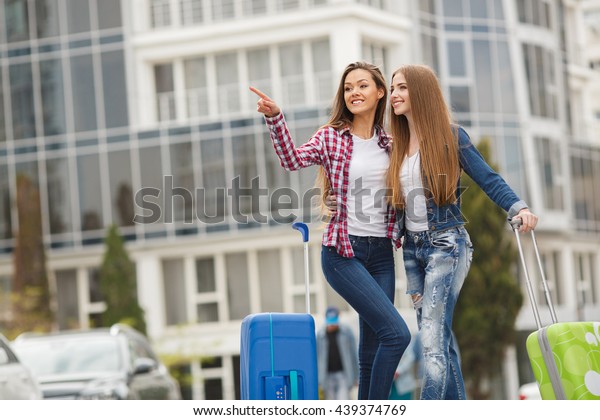 Two young women with\
suitcases. Vacation concept. Car trip. Summer vacation. Best friend\
posing with their luggage. women traveling with suitcases, walking\
on the road