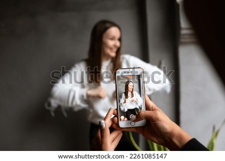  Two young women take photos and videos of each other on smartphone on a terrace