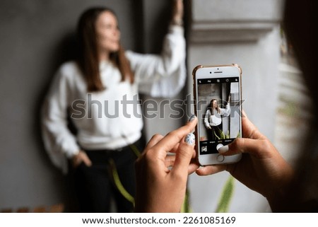  Two young women take photos and videos of each other on smartphone on a terrace