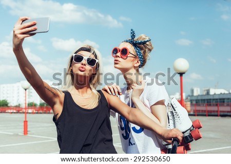 two young women taking selfie with mobile phone. Swag teen girls. Outdoor lifestyle portrait