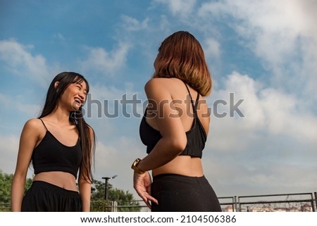 Two young women talking to each other before or after an outdoor workout or jogging session.