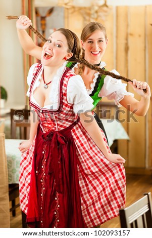 Two young women in traditional Bavarian Tracht in restaurant or pub drawing on hair