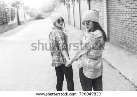 Two young women walking together in the city at sunset. Back view. Black and white
