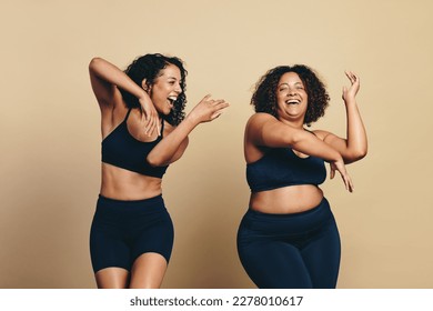 Two young women, wearing sports clothing and full of vitality, dance and exercise together in a studio. Happy female athletes having fun and celebrating their fit lifestyle. - Powered by Shutterstock