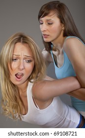 two young women wrestle over grey background