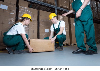 Two Young Workers Lifting Heavy Box In Warehouse