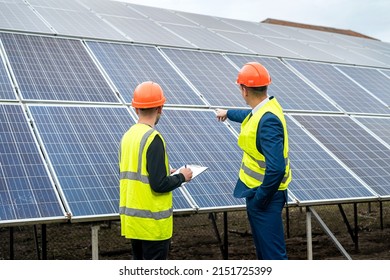 two young workers in overalls and helmets check the installed solar panels. Green electricity concept
