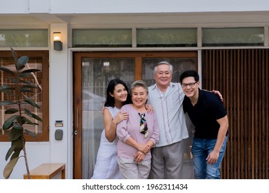 Two-generation Family Standing In Front Of The House Together With Love. Adult Couple Visit To Senior Parents Spending Time Relax And Having Fun On Weekend Vacation Together At Home With Happiness.