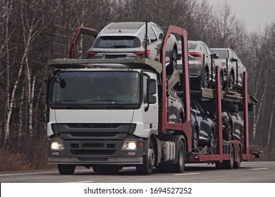 Two-level car carrier truck transports chinese new cars on suburban highway road, front view, delivery autos logistics, automobile transportation