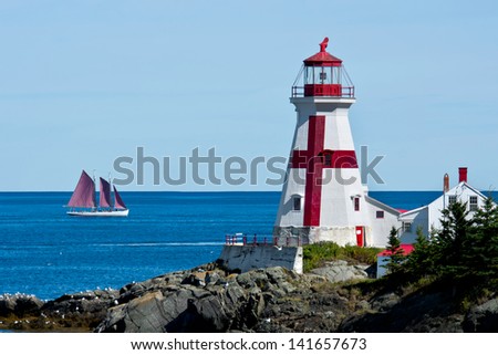 A two-masted schooner sails past the Head Harbour Lightstation on a clear, calm day. Also known as the East Quoddy Head. Campobello Island, New Brunswick, Canada.