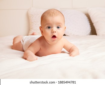 A two-month-old baby on a white blanket lies on his stomach and is surprised. Children's emotions, a surprised child.