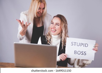 Twoo Female Worker Laughing And Talking About Boss With Sign Stupid Boss.