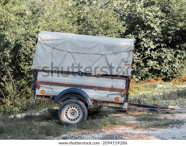A\
two-wheeled trailer with a canopy stands against the background of\
green bushes in the grass on a summer sunny\
day