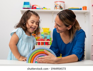 Two-year-old girl and her young kindergarten teacher, both Caucasian, play together in kindergarten, smiling happily - Shutterstock ID 1944904573