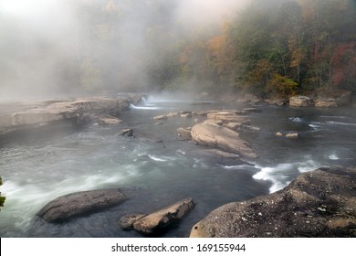 The Tygart River cascades over rocks at Valley Falls State Park in Fairmont, West Virginia, fog over the river in the morning at sunrise