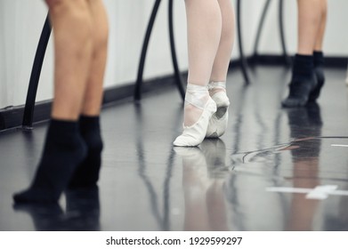 Tying her slippers before performance. Close-up of young ballerina in white tutu tying her slippers while sitting.