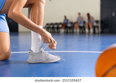 Tying shoelaces, female basketball player preparing for game on court, copy space. Sport, preparation, athlete, footwear, competition, active - Powered by Shutterstock