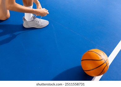 Tying shoelaces on basketball court, woman preparing for game with ball nearby, copy space. Sports, preparation, training, fitness, sneakers, athlete - Powered by Shutterstock