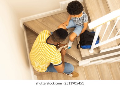 Tying shoes, father helping son on stairs with backpack nearby. Parenting, family, bonding, assistance, childhood, footwear, back to school  - Powered by Shutterstock