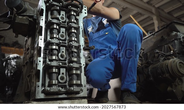 Type of disassembly of car engine. hands of\
professional mechanic in blue uniform, repairing engine. repairman\
working in garage or workshop. person engaged car maintenance. Car\
spare parts. warehouse