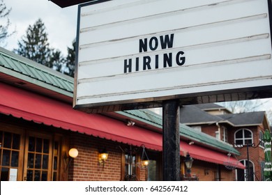 Typical american now hiring sign in black letters over the white background with local small business building  - Shutterstock ID 642567412