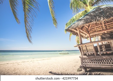 Typical bamboo hut and palm leaves standing at the white sand  beach against background with beautiful sea and cloudless blue sky on a sunny day. Panglao Island, Philippines.