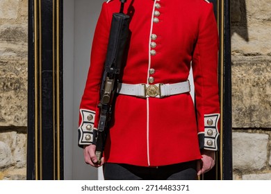 Typical bright red and white jacket of the British Royal Guard with automatic rifle standing sentry.