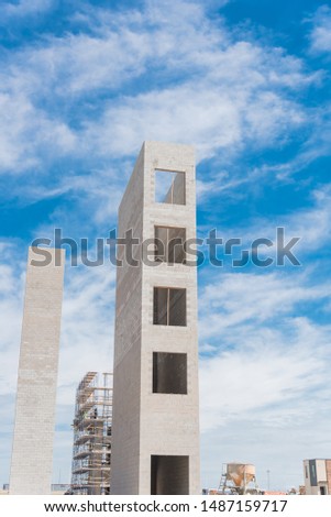 Typical construction site of new condominium building in Texas, America with elevator shaft and metal scaffolding system. Looking up view of concrete elevator tower under cloud blue sky