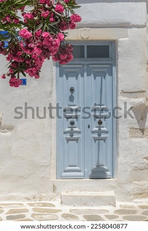 Typical Cycladitic architecture of a whitewashed facade of a house  with a typical traditional door and  blooming flowers in Parikia, Paros island, Greece.