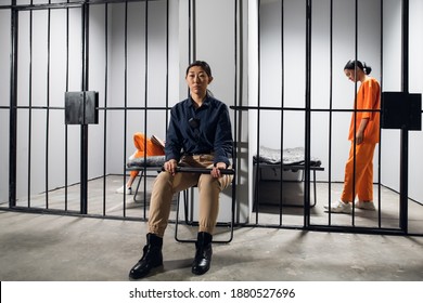 A Typical Day In A Women's Prison. A Bored Female Guard In Uniform Sits Near The Cells With Female Prisoners