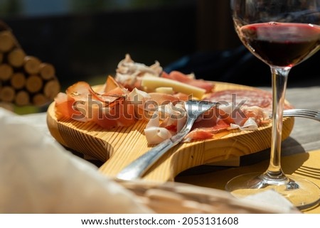 Typical eastern Italy appetizer made of red wine and a cutting board with ham and cheese, close up view, Friuli Venezia Giulia tradition, eating  lunch together concept