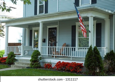 A Typical Front Porch Of A Home In A Small Town In  The U.S.A. Featuring An American Flag Proudly Flying And A Porch Swing To Enjoy The Spring Day.