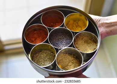 A Typical Indian Spice Box With Multiple Containers. Close Up Of A Hand Holding Container.