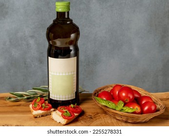 The typical Italian bruschetta with toasted bread, tomato, basil and olive oil on a wooden cutting board and next to it a bottle of extra virgin olive oil