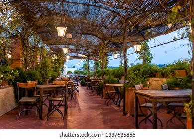 Typical Italian Rooftop Restaurant Wooden Tables In Tuscany With Covered Roof Pergola Vine Canopy With Empty Seats, Chairs And Nobody In Rustic Romantic Architecture