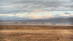 Typical Landscape At Israel Jordan Border As Seen From Car Driving On Highway 90. Flat Dry Desert With Small Mountains At Jordanian Side, Sun Shines Through Evening Clouds