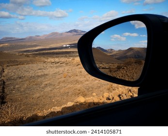 Typical landscape of Lanzarote island (Canary islands) with volcanoes covered with dry plants and mountains and blue sky reflected in rear window of a car. Active lifestyle and leisure in mountains - Powered by Shutterstock