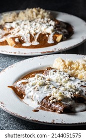 Typical Mexican Food. Mole Enchiladas. Fried Tortillas With Chicken Inside And Mole Sauce On Top. 2 White Plates On A Black Background